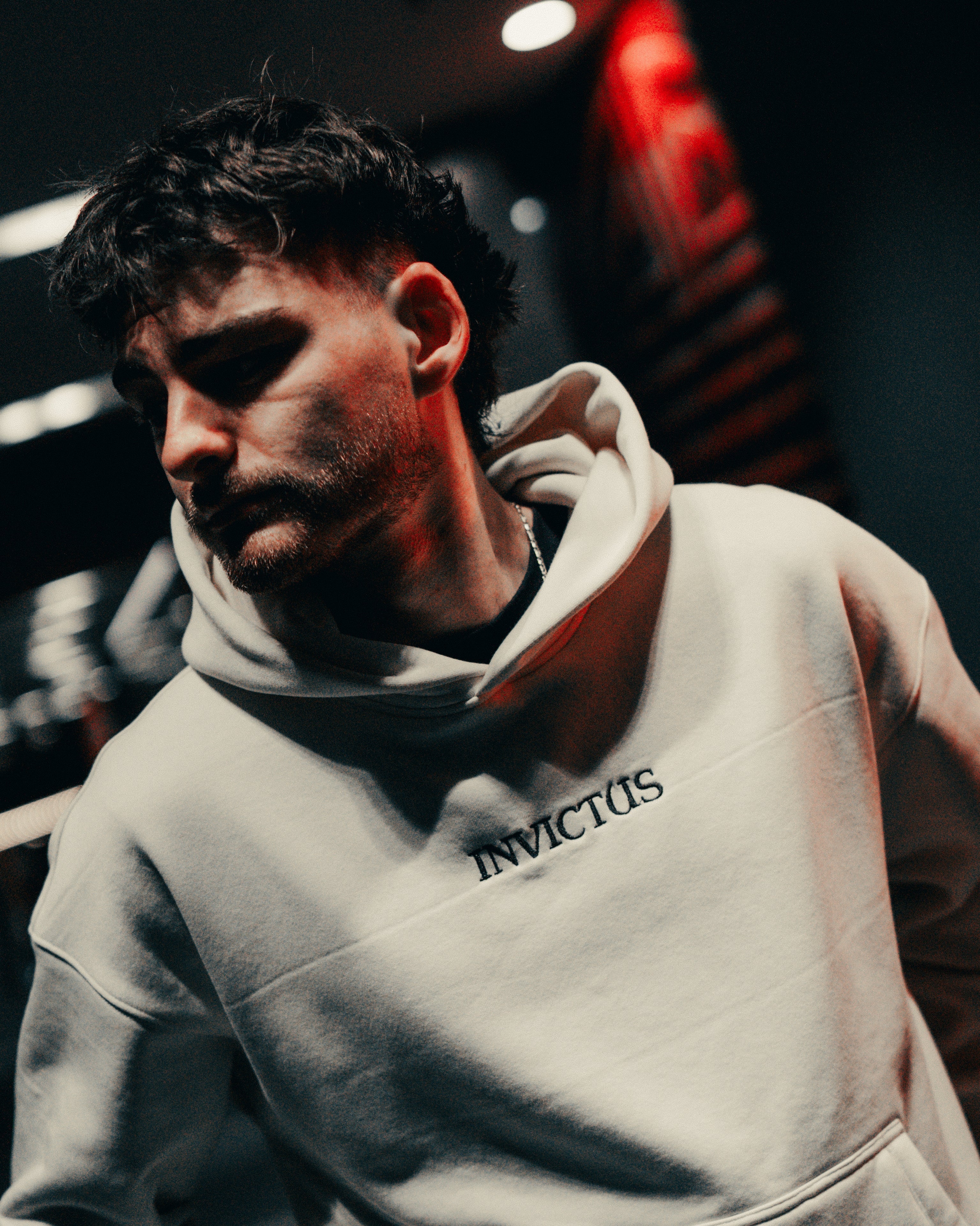 Man wearing an off-white hoodie with 'INVICTUS' branding in a dimly lit setting.