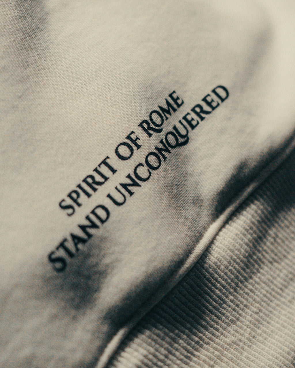 Text 'Spirit of Rome Stand Unconquered' on an off-white hoodie