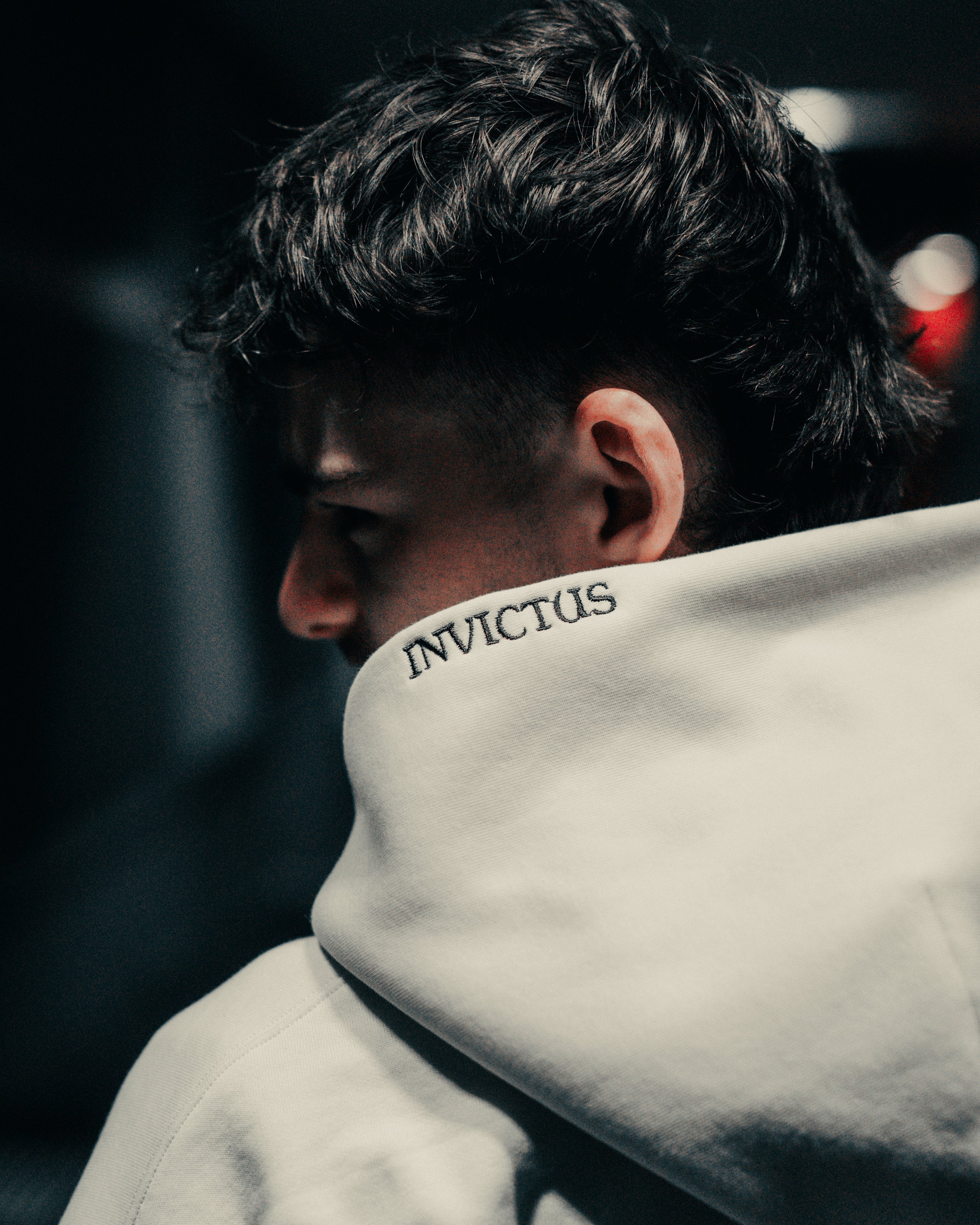 Person wearing an off-white hoodie with embroidered 'INVICTUS' text, facing away from the camera.