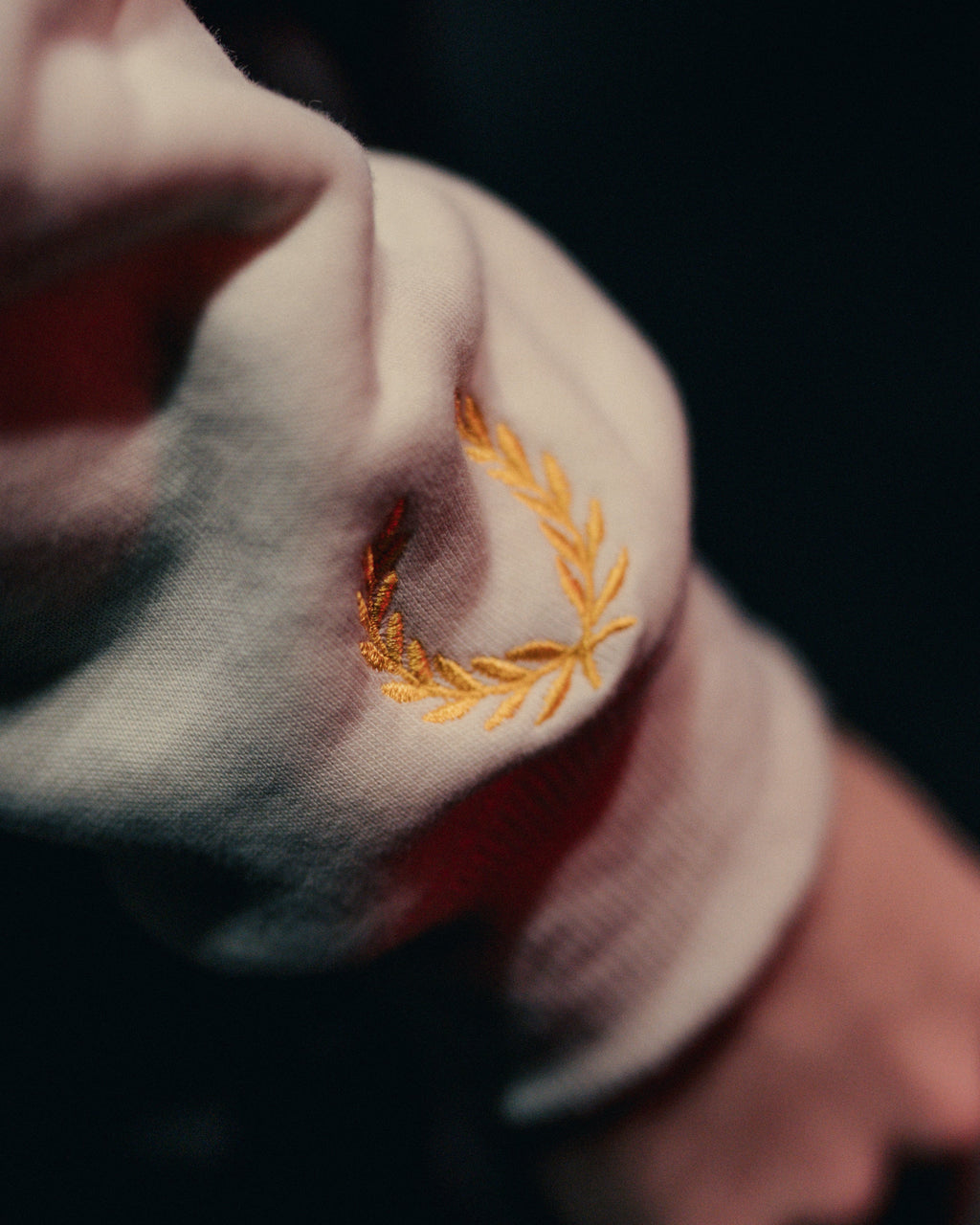 Close-up of a person wearing an off-white hoodie with an embroidered wreath on the sleeve.