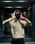 Person wearing an off-white hoodie with 'INVICTUS' branding in a dimly lit indoor setting.