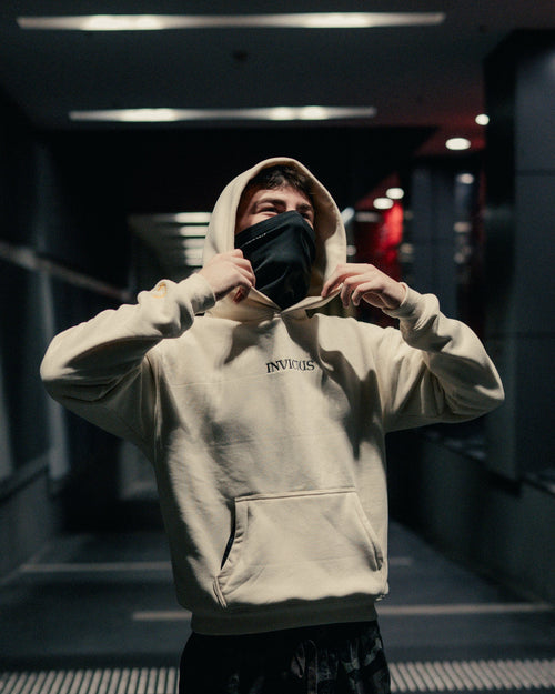 Person wearing an off-white hoodie with 'INVICTUS' branding in a dimly lit indoor setting.
